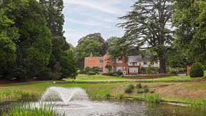 A large brick house with a pond in front, surrounded by lush greenery and trees. - Donnington Hotel, Spa & Golf (Newbury)