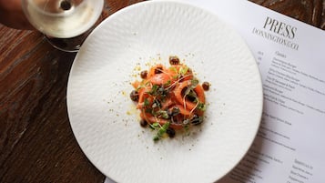 A menu with various dishes listed, a white plate with food, a glass of white wine, and a copper candle holder on a wooden table.