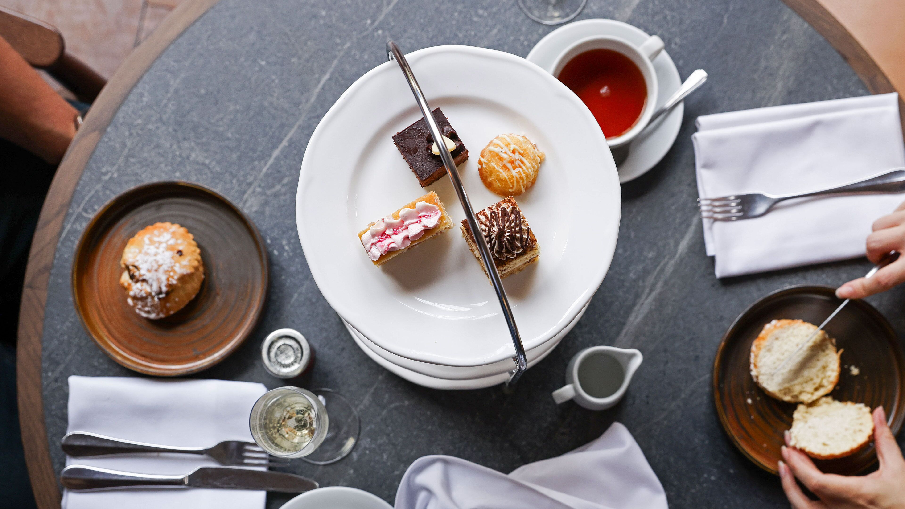 Une table dressée pour un repas, avec divers desserts, une tasse de thé et un verre d’eau.