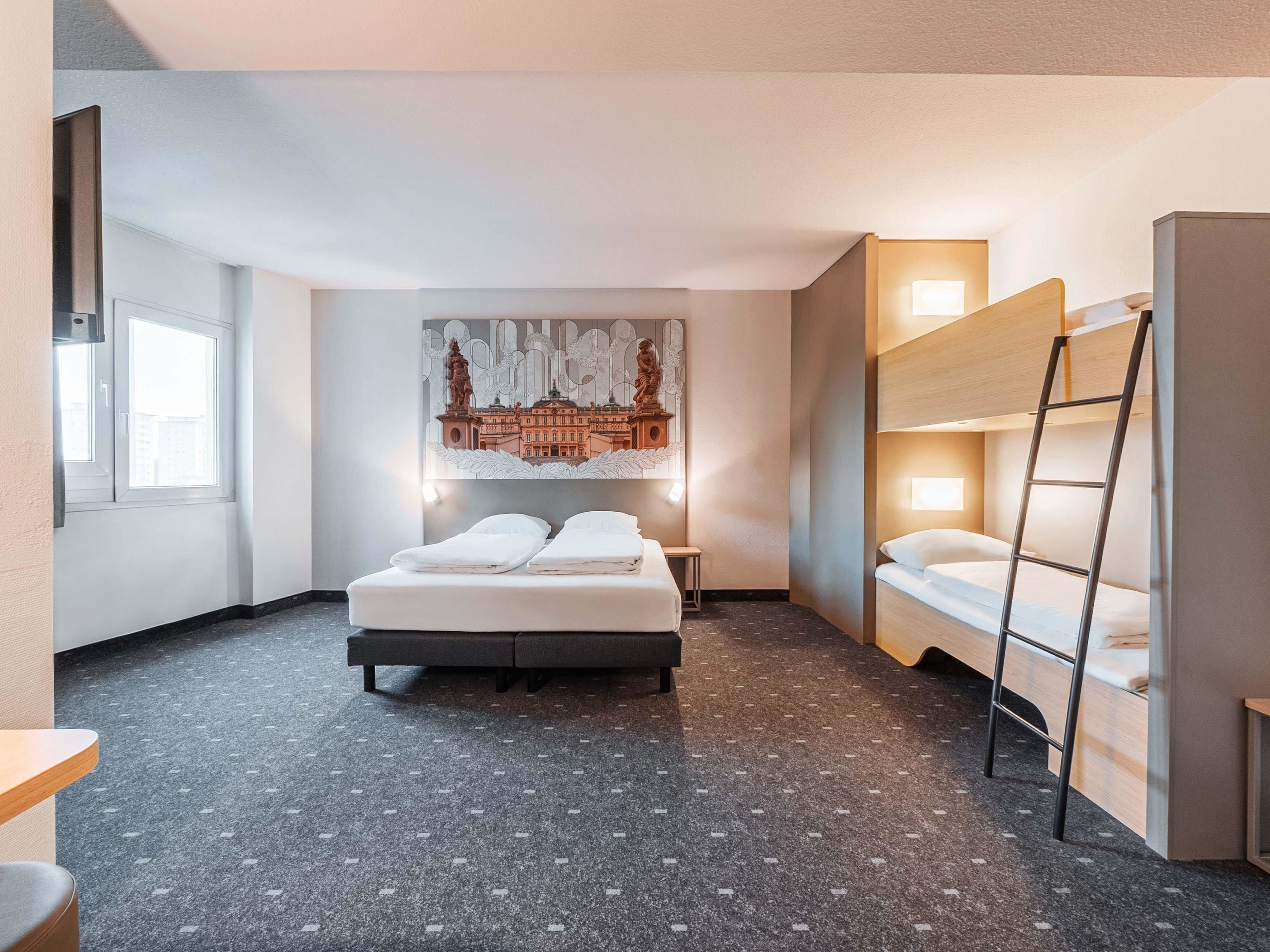 Une chambre d’hôtel moderne avec un grand lit, un lit superposé, une échelle, une petite table et une œuvre d’art accrochée au mur.