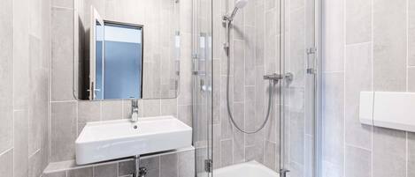 Un baño moderno con ducha de vidrio, lavamanos blanco y espejo.