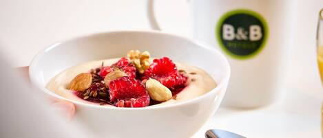 A bowl of yogurt with fruits and nuts, a spoon, and a mug with a logo.