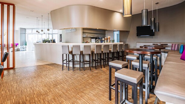 A modern bar area with wooden flooring, bar stools, and a curved counter. - B&B HOTEL Rastatt (Rastatt)
