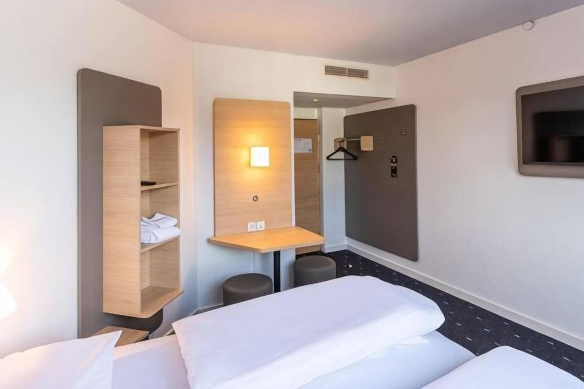 Une chambre d’hôtel avec un lit, une armoire en bois, une petite table et un miroir.