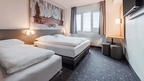 A hotel room with two beds, a large wall mural, a window with curtains, a flat-screen TV, and a small table with a lamp. - B&B HOTEL Rastatt (Rastatt)