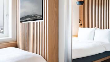 A modern hotel room with a wooden slat wall design, a large mirror, and a bed with a view of a cityscape through a window.