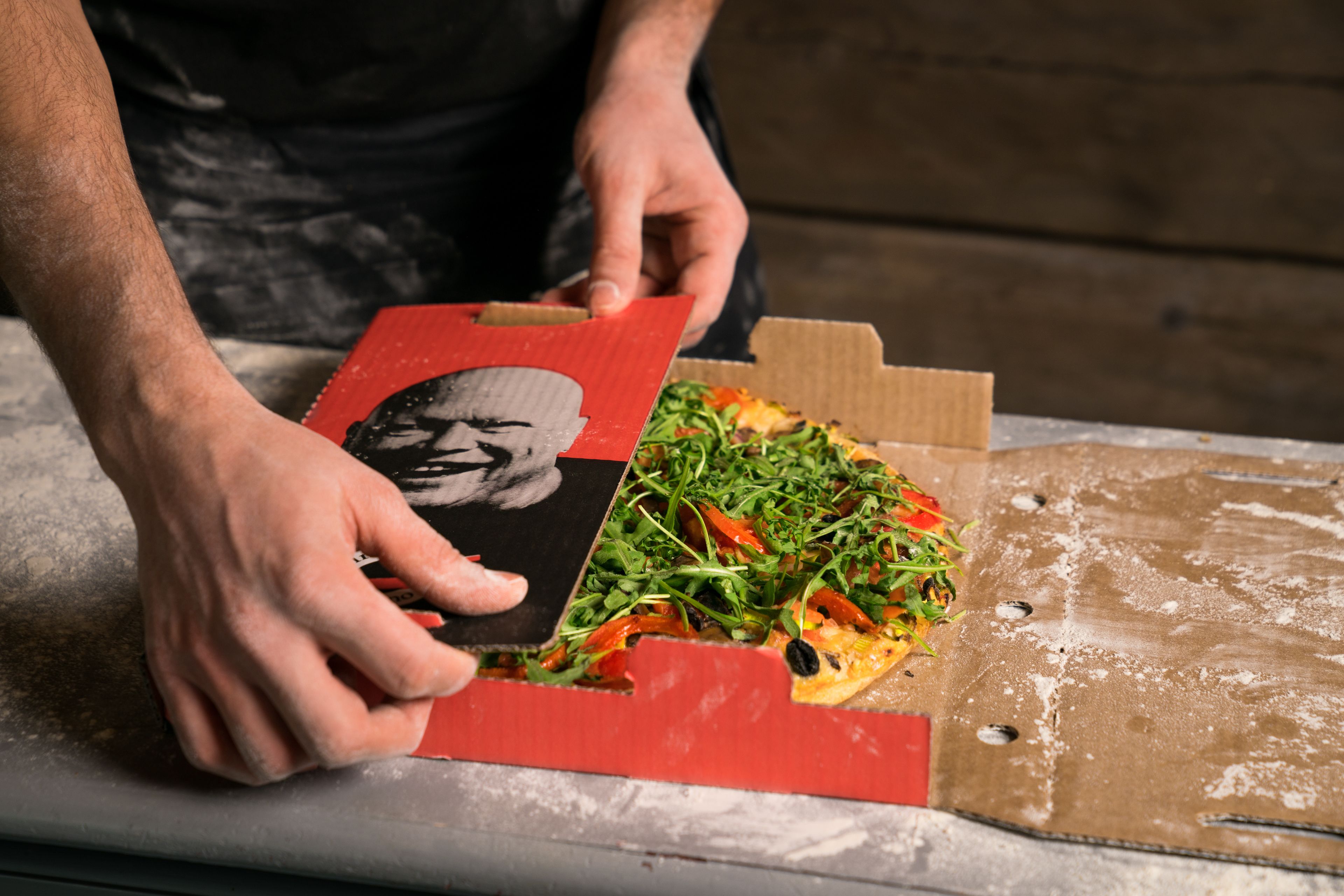 A person holding a pizza box with a picture of a man on it.