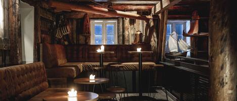 A rustic interior with wooden walls, leather seating, and small round tables with candles.