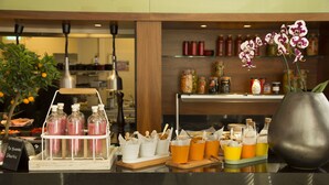 A counter with a fruit stand, drink dispensers, and a vase with orchids.