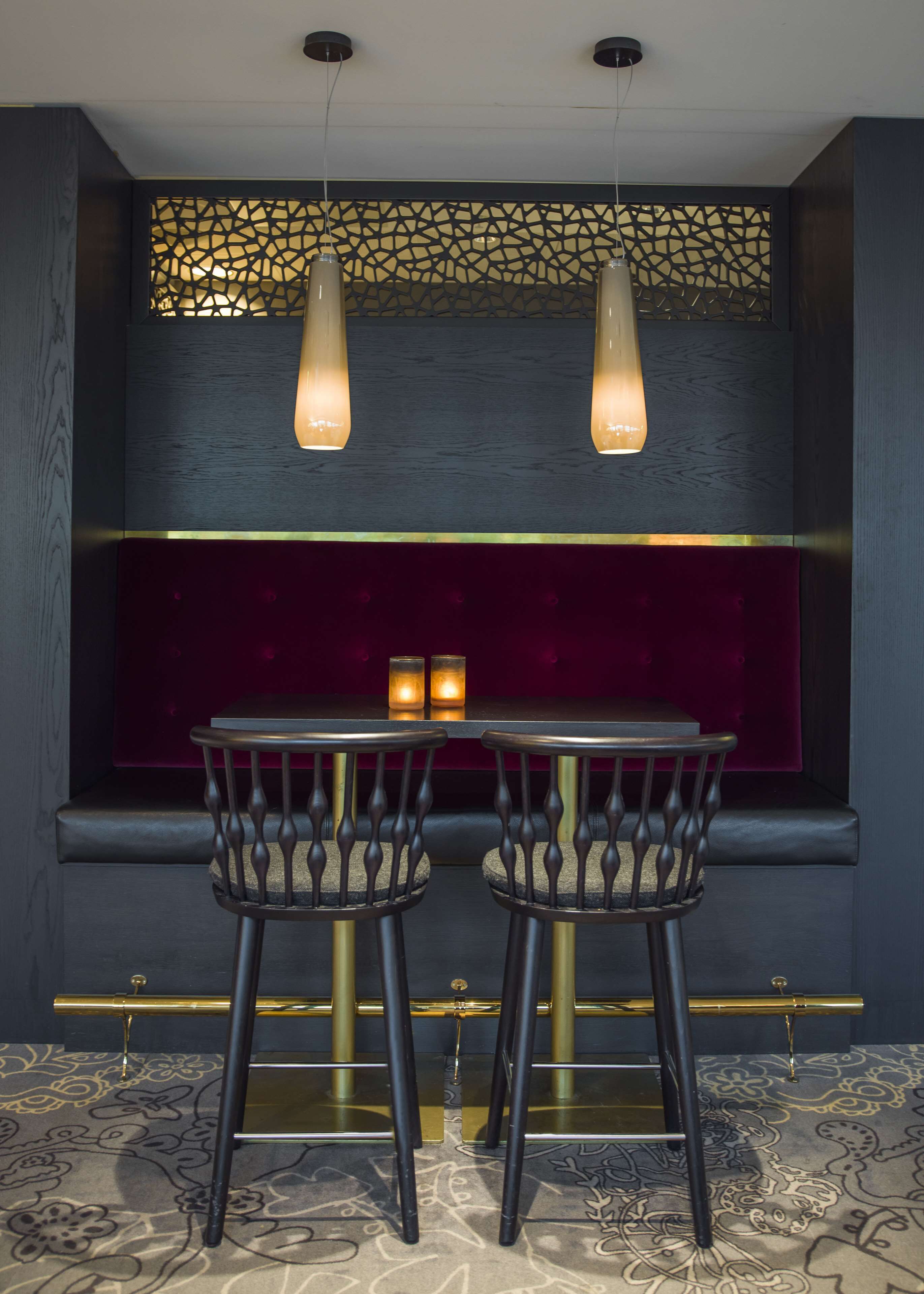 A dark-themed dining area with a table and two chairs, a decorative wall, and hanging pendant lights.