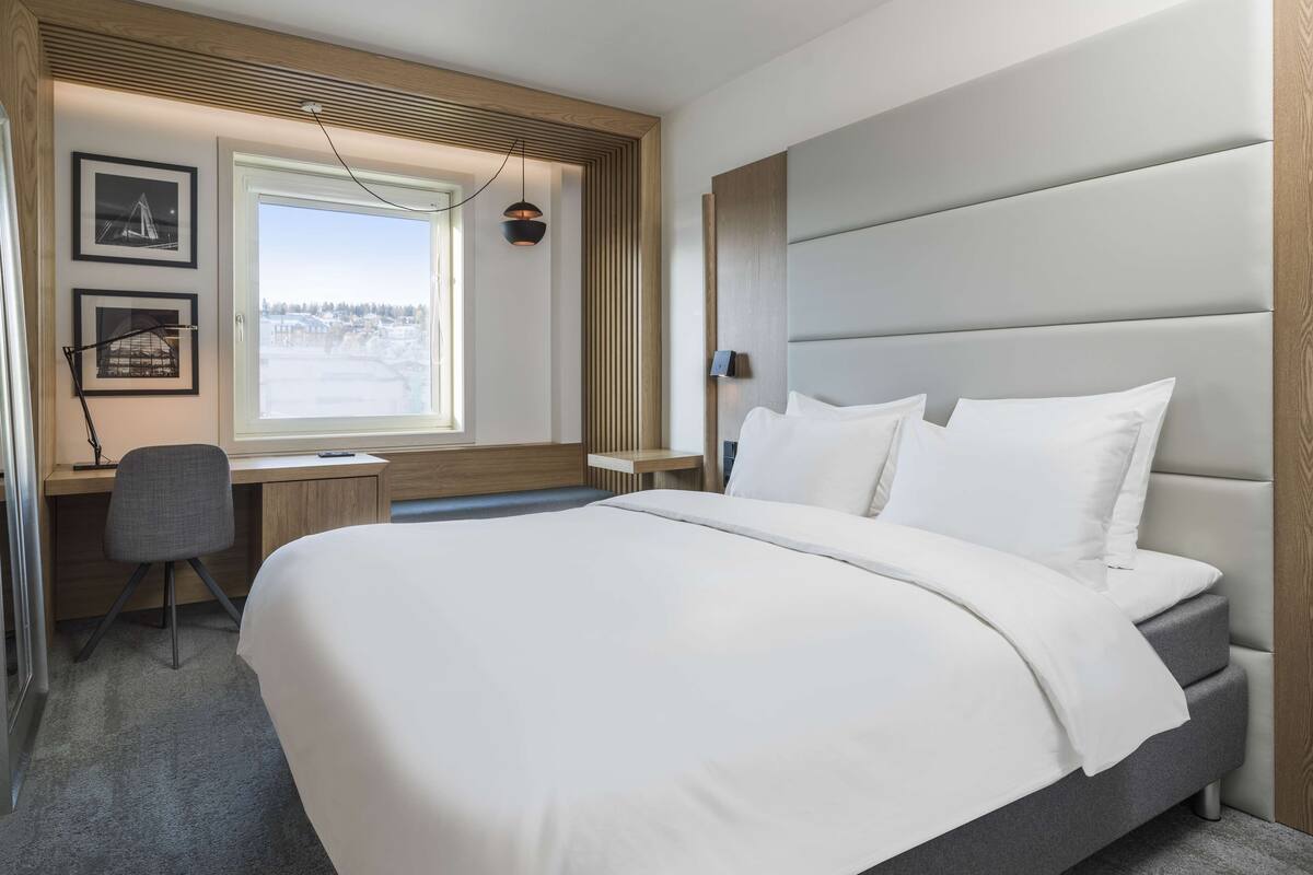 A modern hotel room with a large bed, a desk, and a chair.
