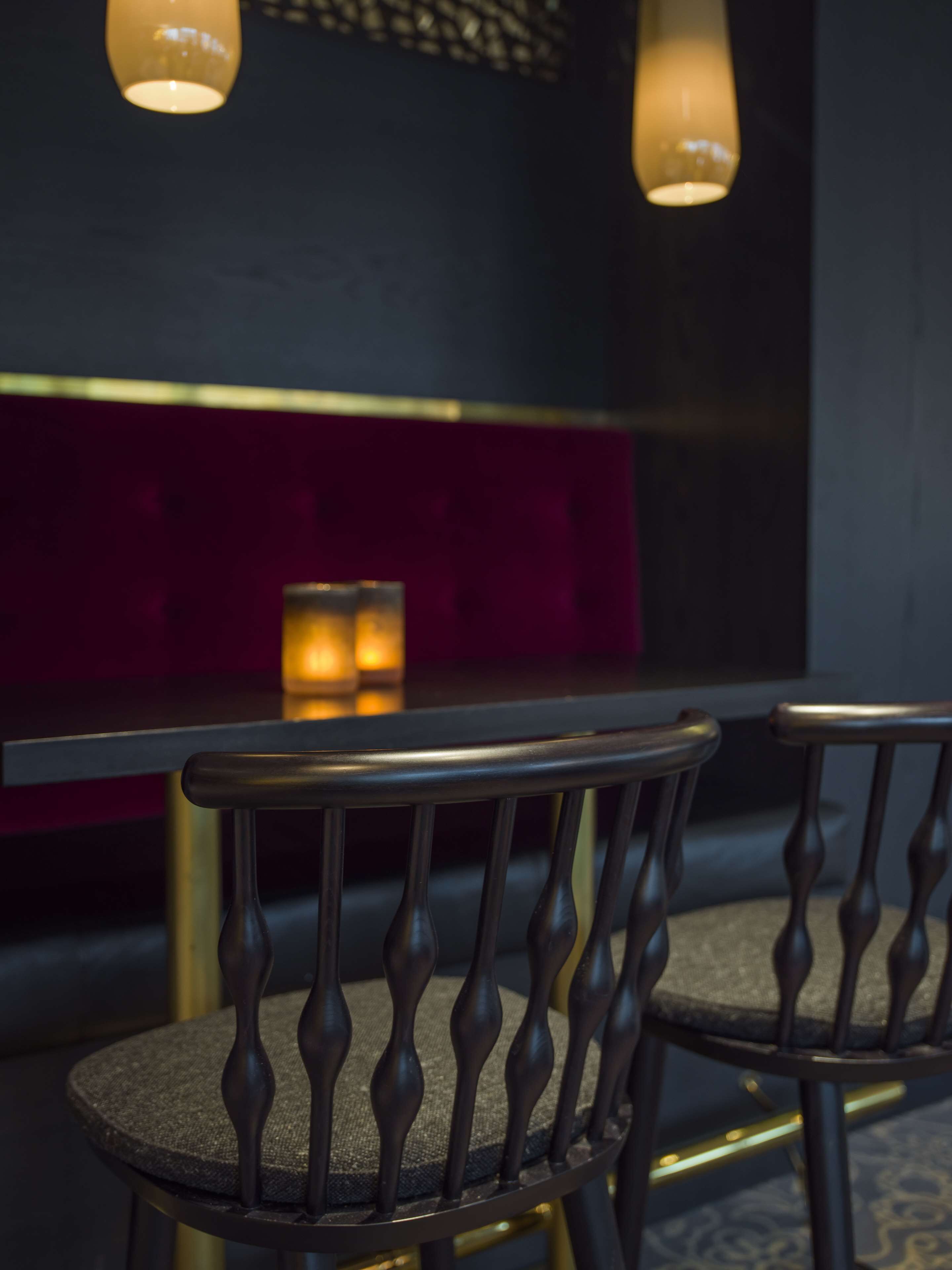 A dining area with a table and chairs, a candle on the table, and a red upholstered bench in the background.