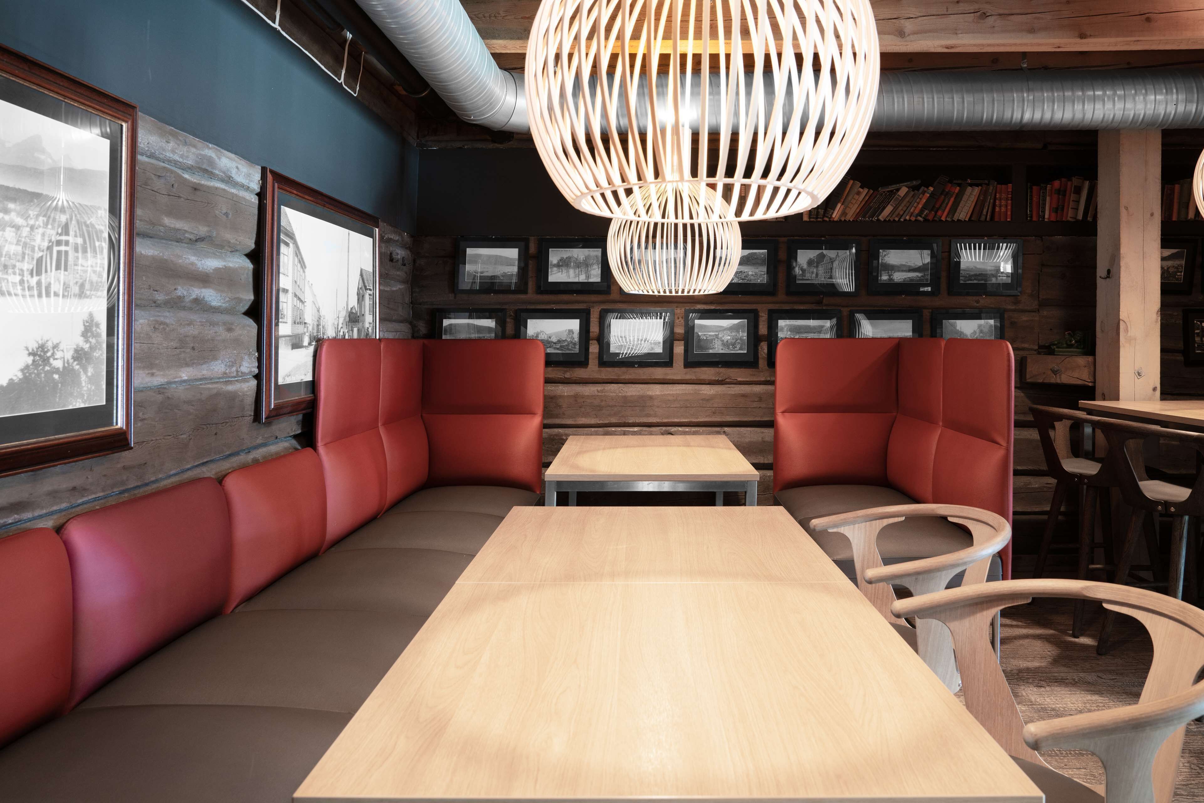 A cozy restaurant with wooden walls, red cushioned seating, and a large wooden table.
