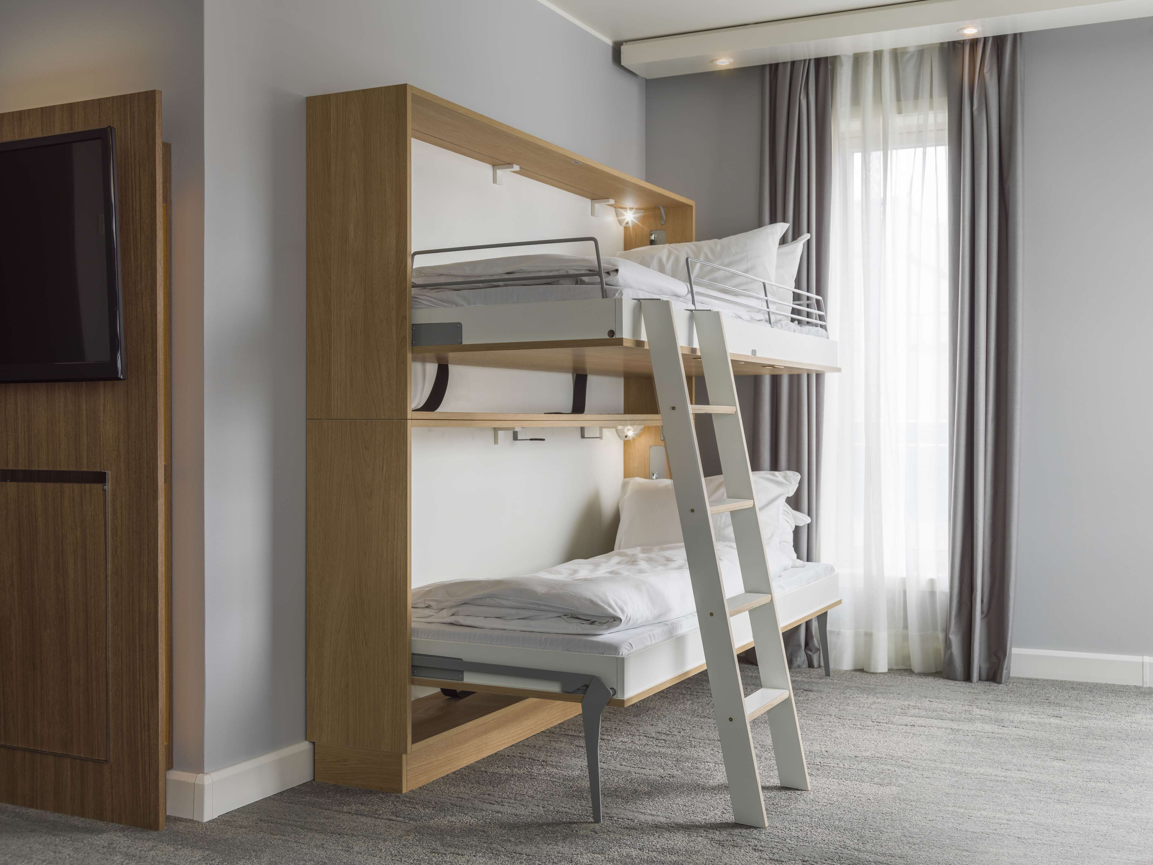 Ein Stockbett mit einer Leiter, ein an einer Holzplatte montierter Fernseher und ein Fenster mit Vorhängen.