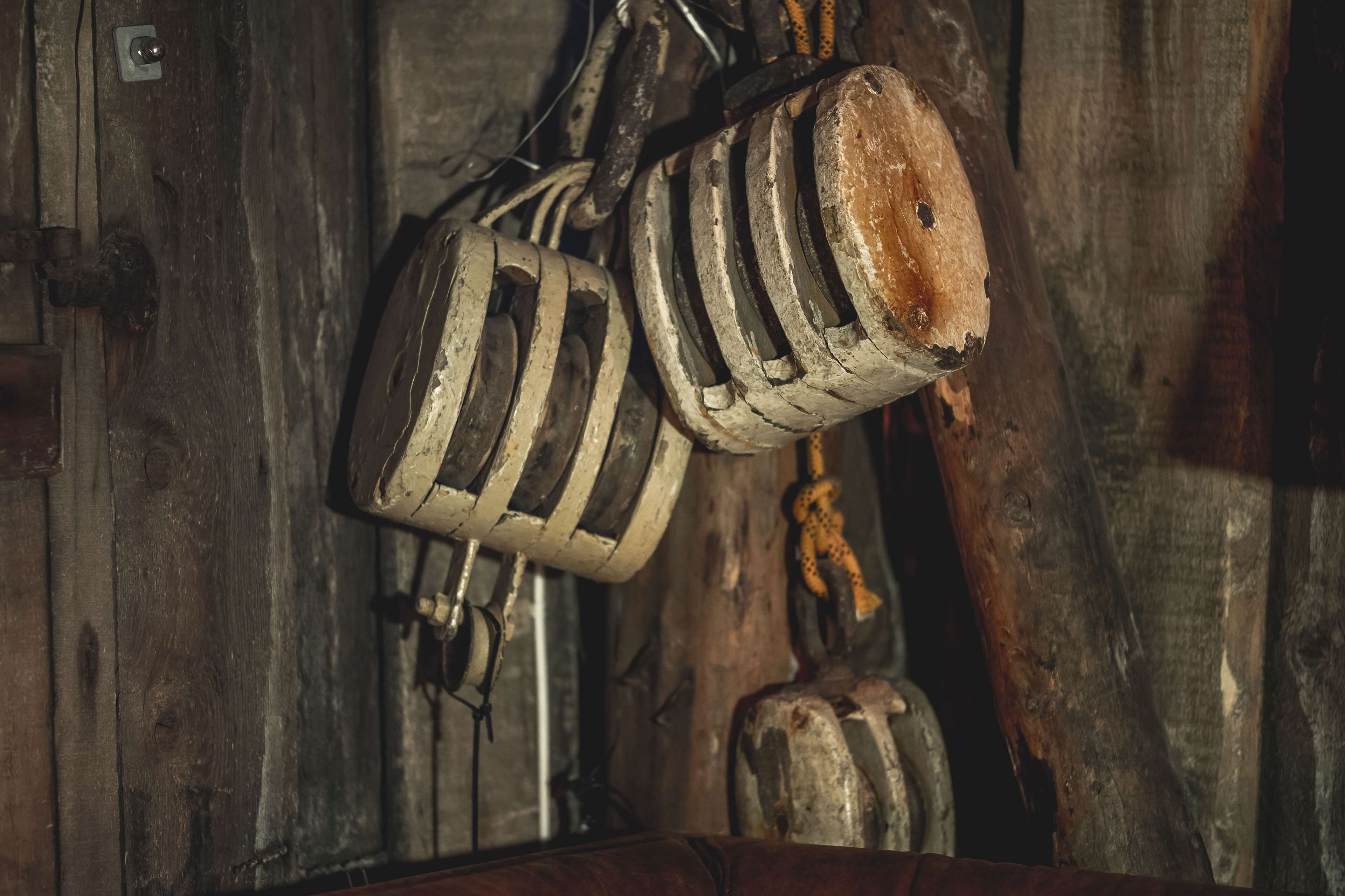 Un interior rústico de madera con un objeto colgante de madera, posiblemente una herramienta o adorno, y un taburete pequeño y desgastado.