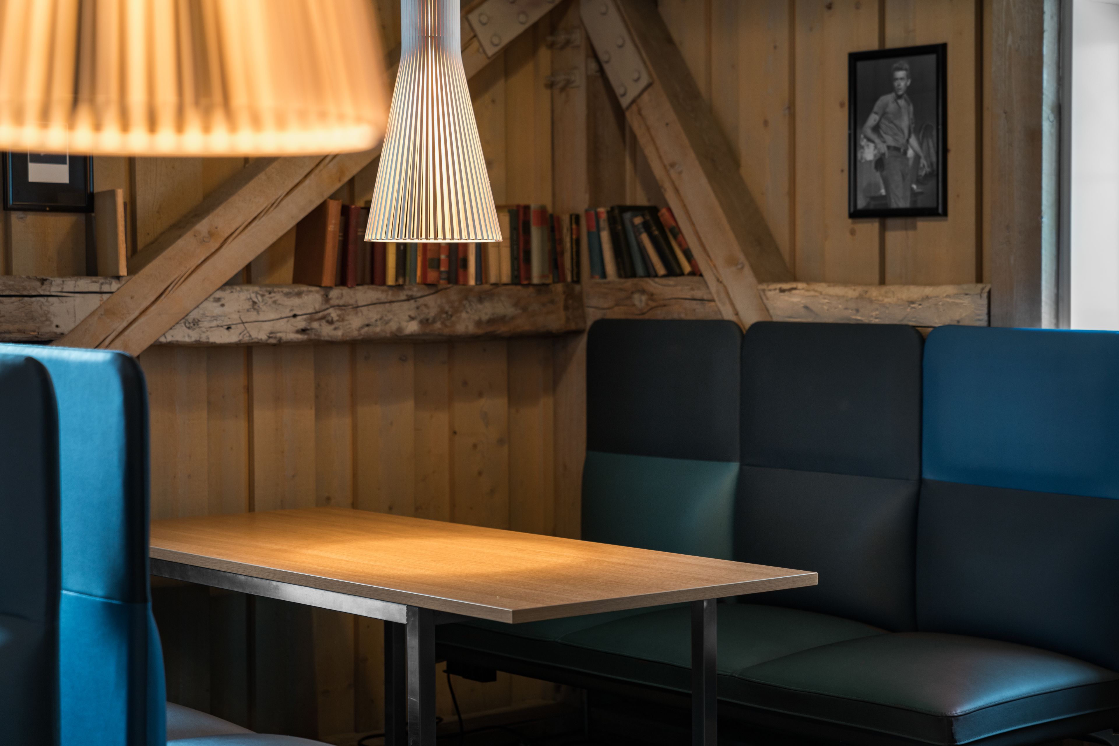 A cozy seating area with a wooden table and benches, a hanging light fixture, and a bookshelf with books.