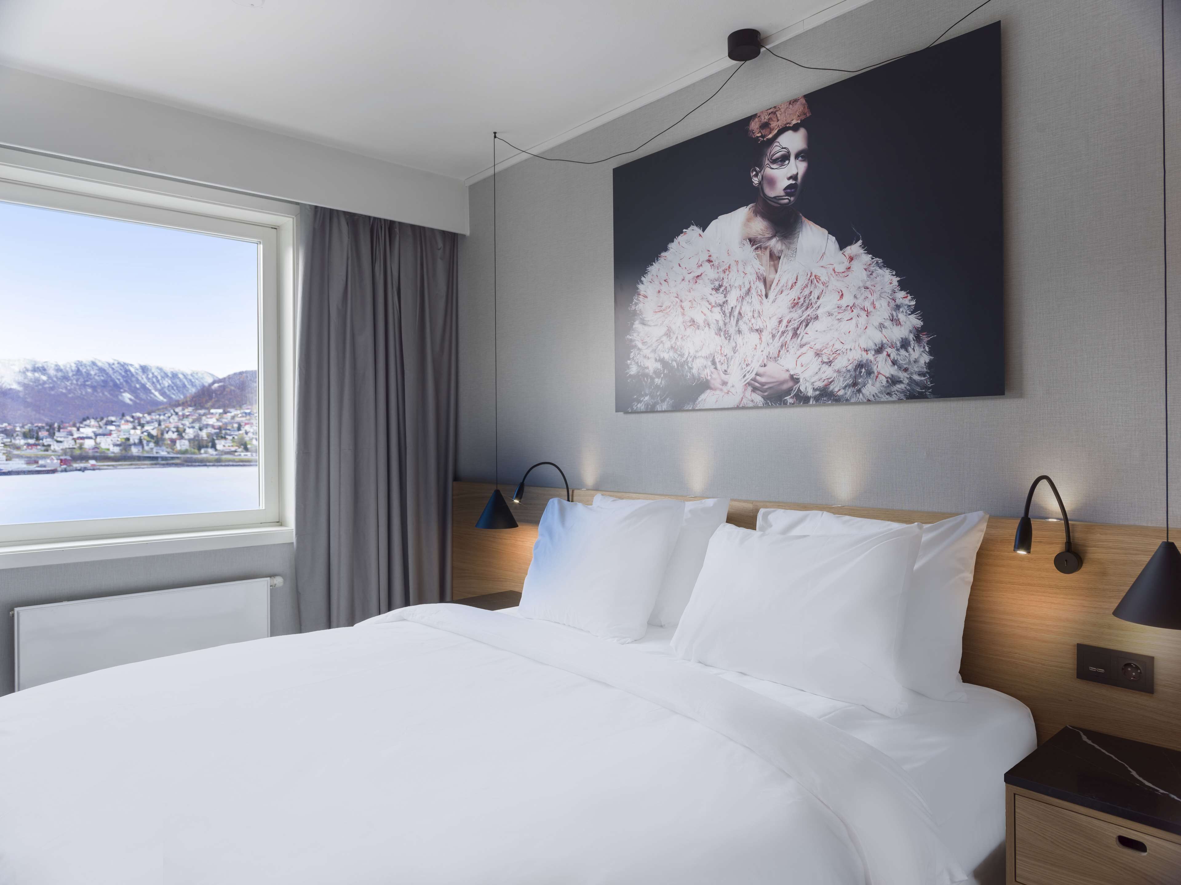 Habitación de hotel con una cama grande, vista a un paisaje nevado y un cuadro en la pared.