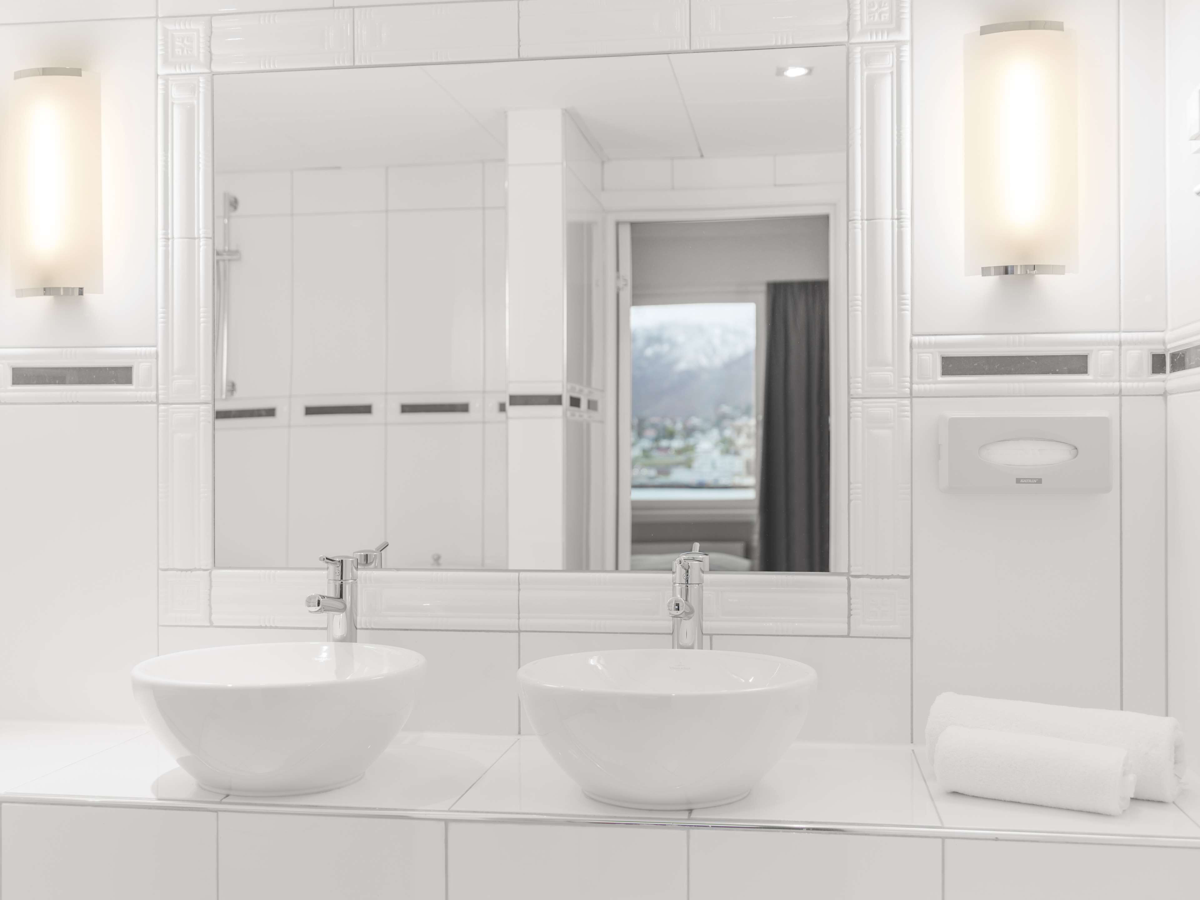 A modern bathroom with two large white sinks, a large mirror, and a view of a snowy landscape through the window.
