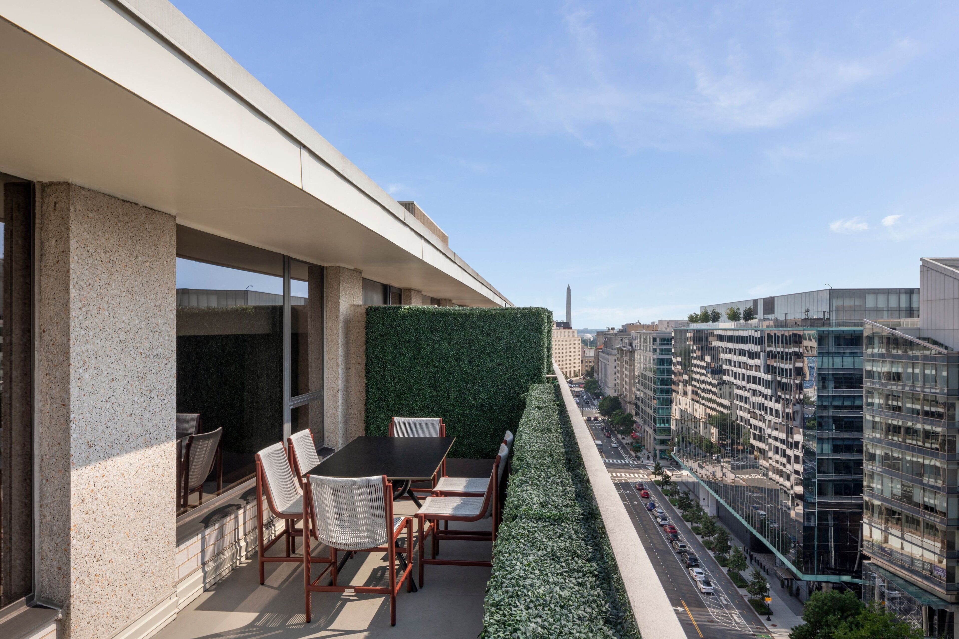 A modern outdoor seating area with a table and chairs, a green wall, and a view of the cityscape.
