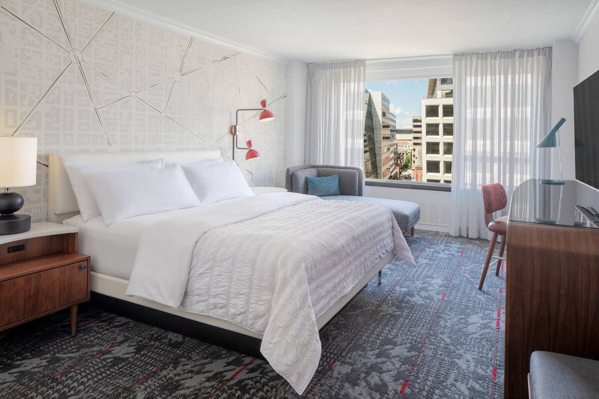 A hotel room with a large bed, a desk, a chair, and a TV.