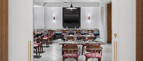 Zona pranzo moderna con tavoli apparecchiati, una grande TV a schermo piatto montata a parete e lampadari a sospensione.
