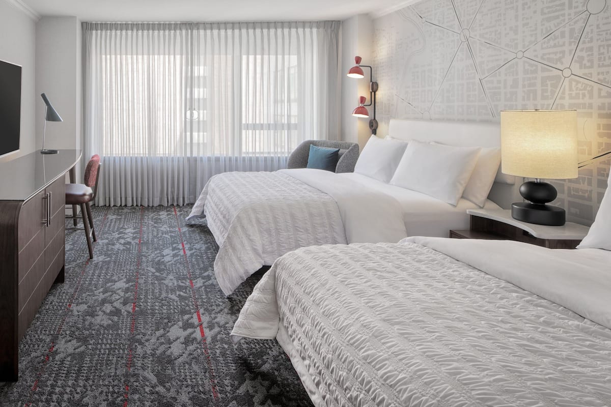 A hotel room with two beds, a TV, a desk, and a chair.