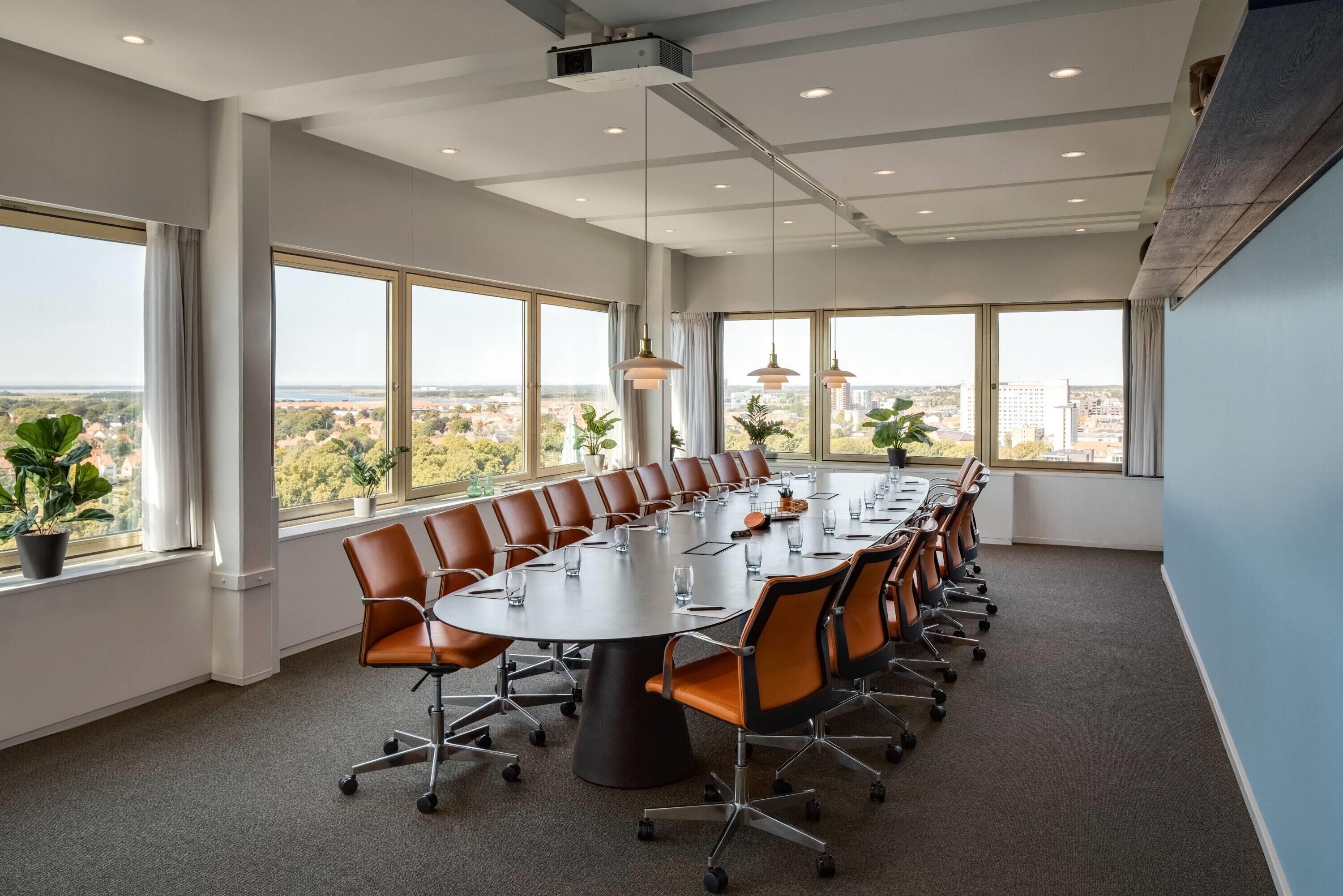 A conference room with a long table, multiple chairs, and large windows offering a city view.