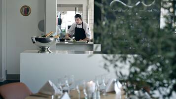 Interior de restaurante con un chef preparando comida, un menú en pizarra y un comedor listo para los comensales.