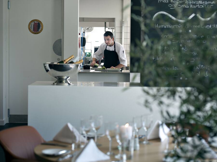 Interior de restaurante con un chef preparando comida, un menú en pizarra y un comedor listo para los comensales.