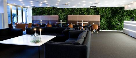 A modern lounge area with sofas, tables, and a green wall.