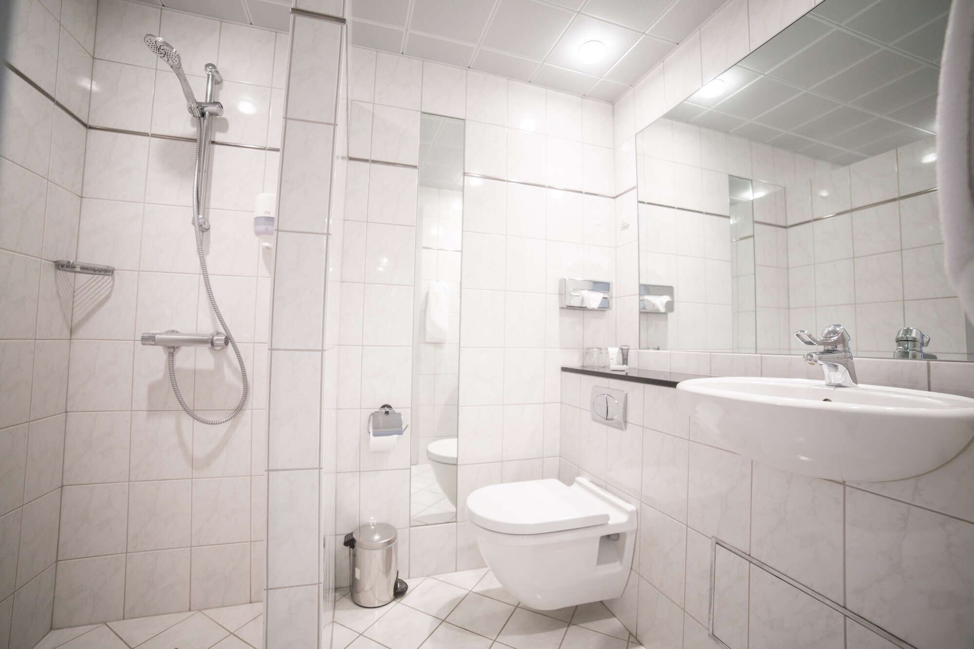 A modern bathroom with a shower, toilet, sink, and a trash bin.