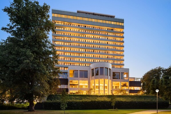 A modern multi-story hotel with a central courtyard, large windows, and a well-maintained garden. - Comwell Hvide Hus Aalborg, Dolce by Wyndham (Aalborg)