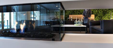 Un interior moderno con un separador de vidrio, una zona de estar con sofá y mesa, y una chimenea visible.