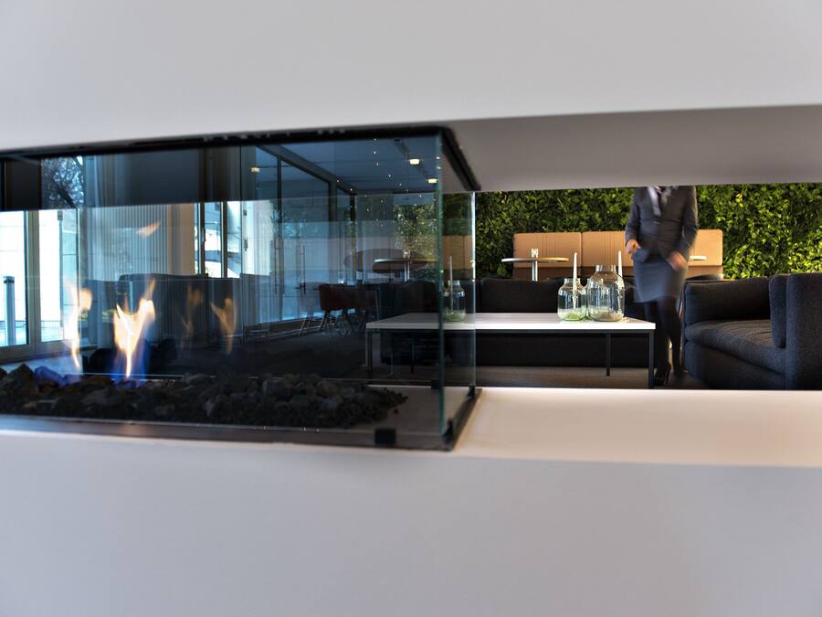 Un interior moderno con un separador de vidrio, una zona de estar con sofá y mesa, y una chimenea visible.