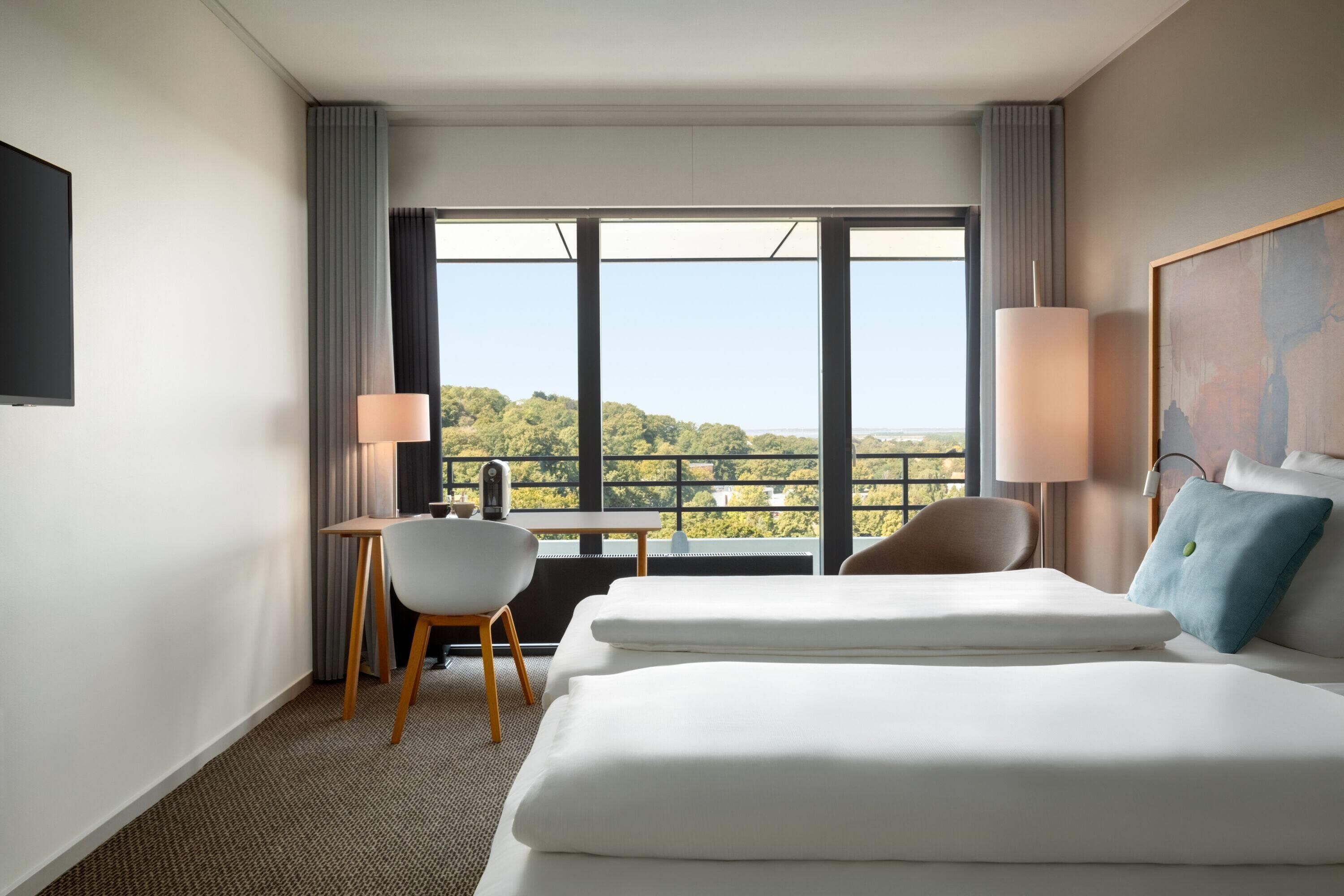 A hotel room with a large bed, a desk, a chair, and a view of the outdoors.