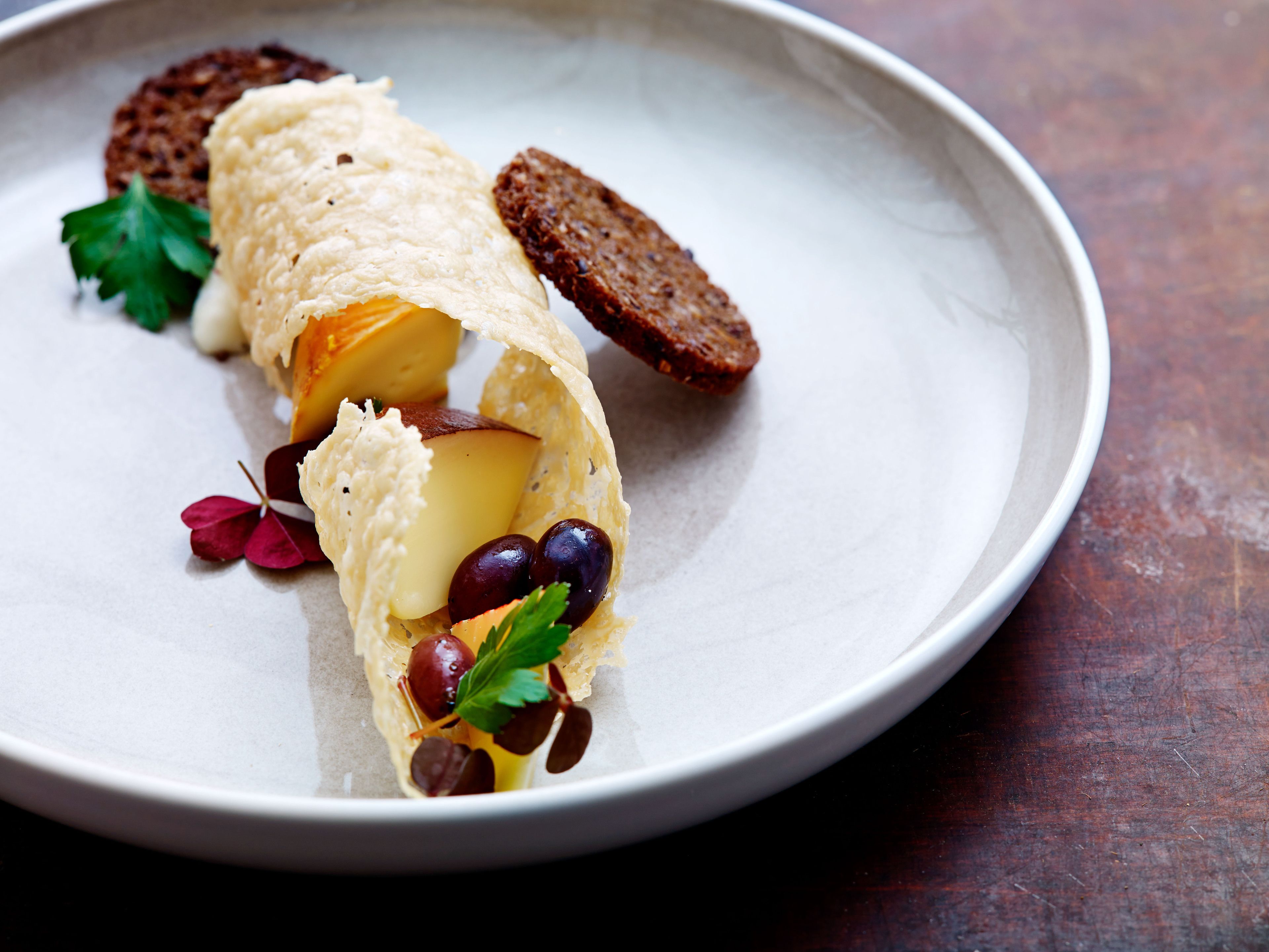 A plate with a rolled pastry, slices of bread, olives, and a garnish.