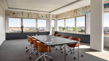 A conference room with a large table, orange chairs, and large windows with city views.