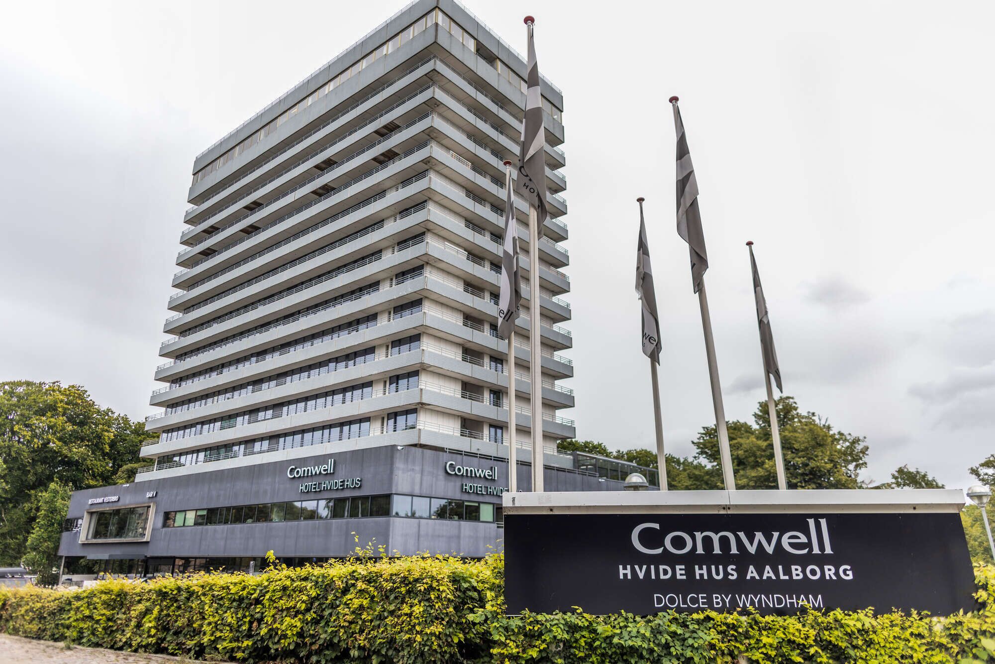 A modern hotel building with multiple balconies and a sign indicating 'Comwell Hotel Hvide Hus Aalborg.'