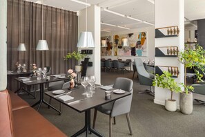 A modern dining area with tables set for service, a bar area, and a casual seating space with potted plants. - Comwell Hvide Hus Aalborg, Dolce by Wyndham (Aalborg)