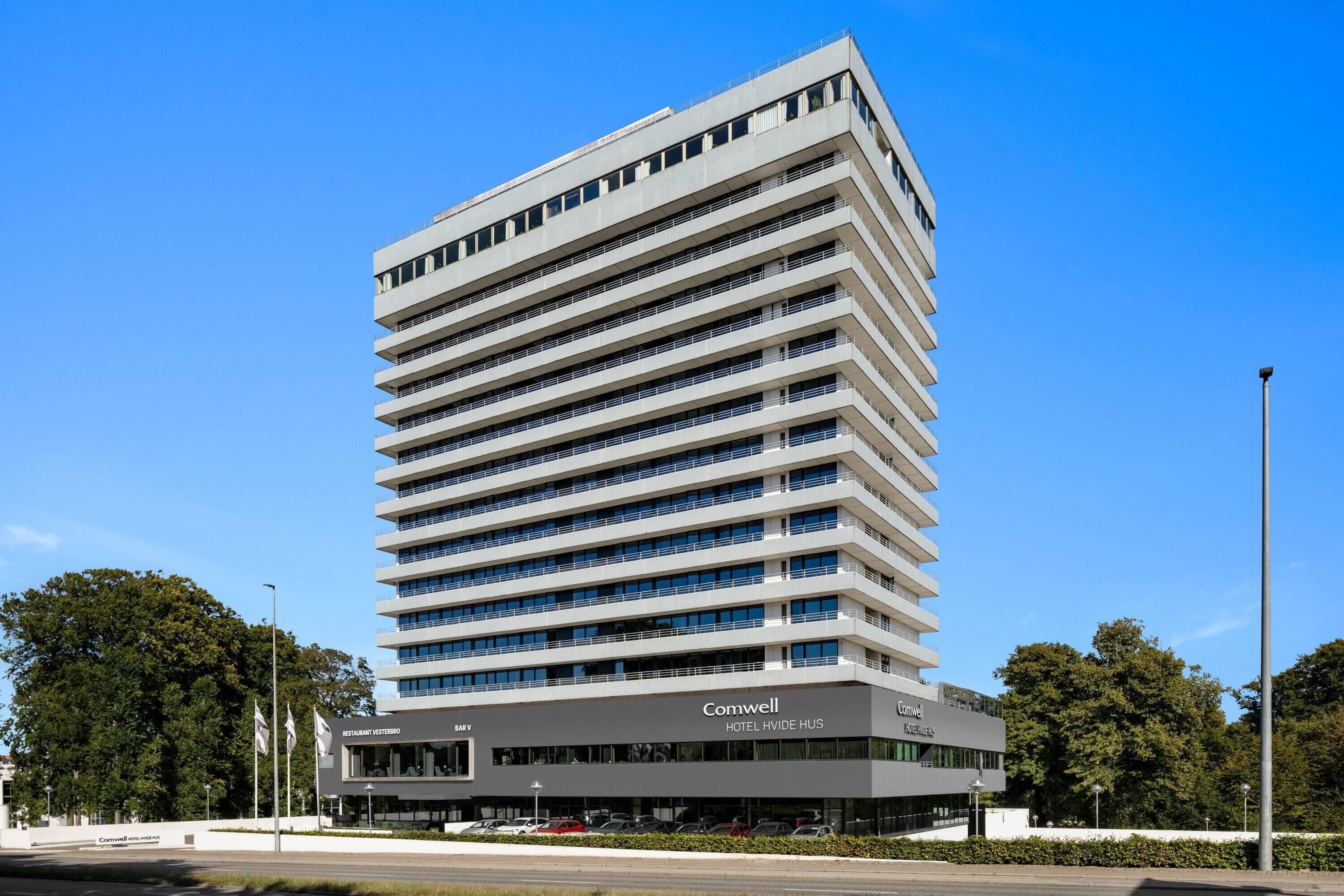 A modern hotel building with multiple floors, a flat roof, and a prominent signage for 'Comwell Hotel Hvide Hus'.