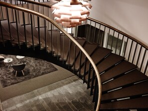 A spiral staircase with a modern design, featuring a metal railing and a unique, geometric pendant light.