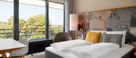 A hotel room with a large window, a bed with white linens, a desk, and a chair.