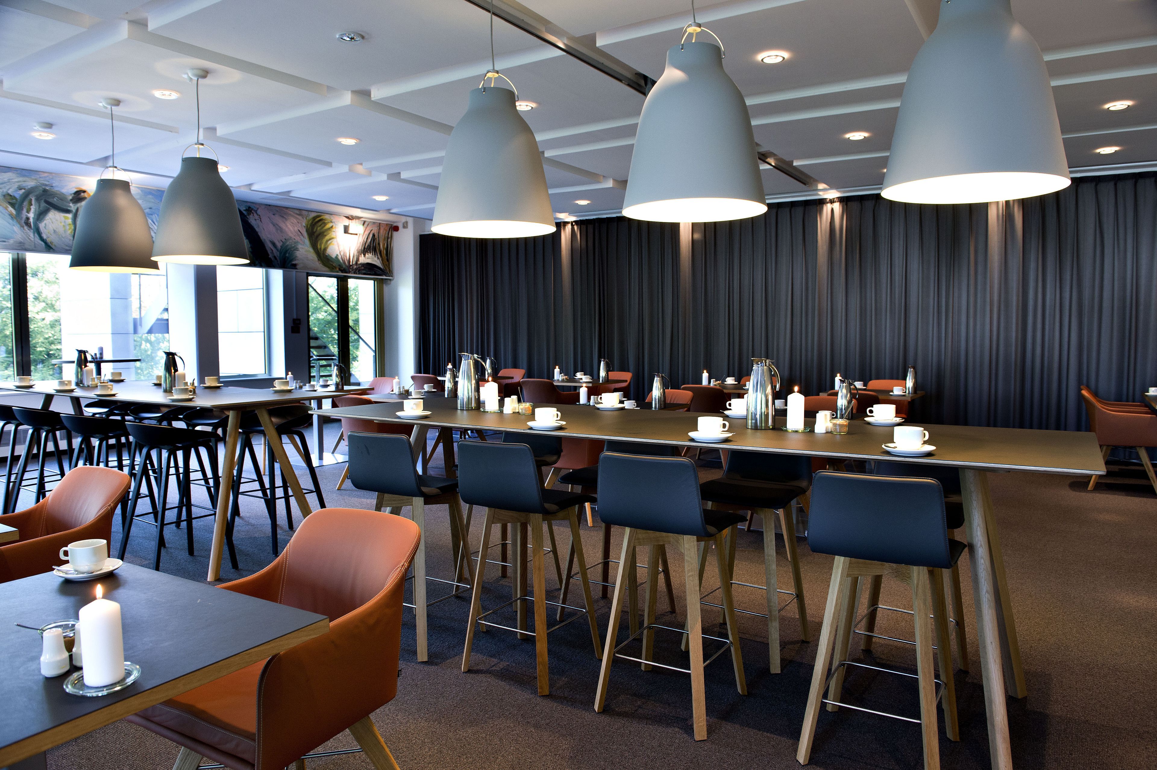 A modern dining area with long tables, chairs, and pendant lighting.