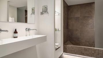 A modern bathroom with a white sink, a mirror, a hand soap dispenser, and a shower area with brown tiles.