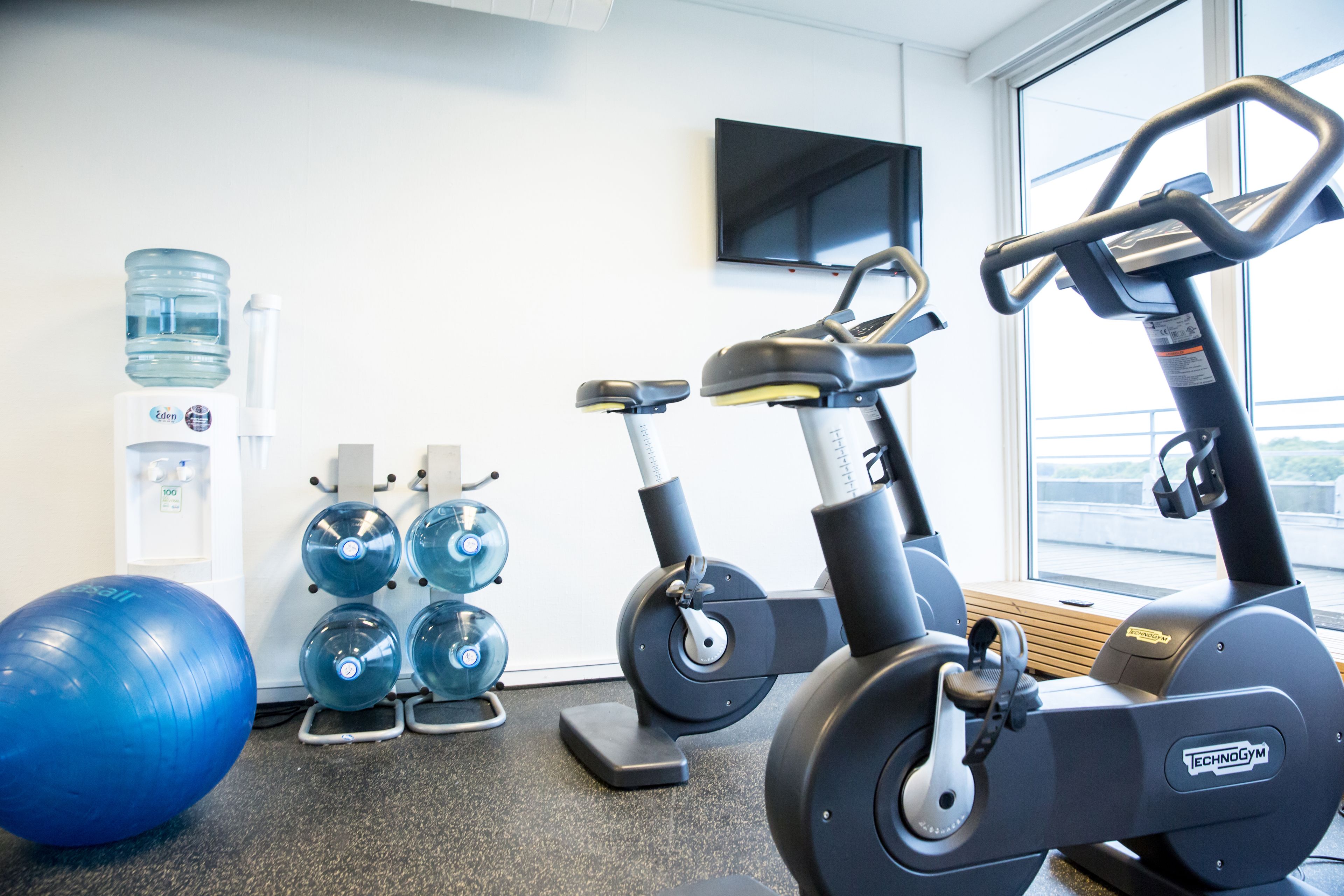 Ein Fitnessraum mit Trainingsgeräten, einem Wasserspender und einem Fernseher an der Wand.