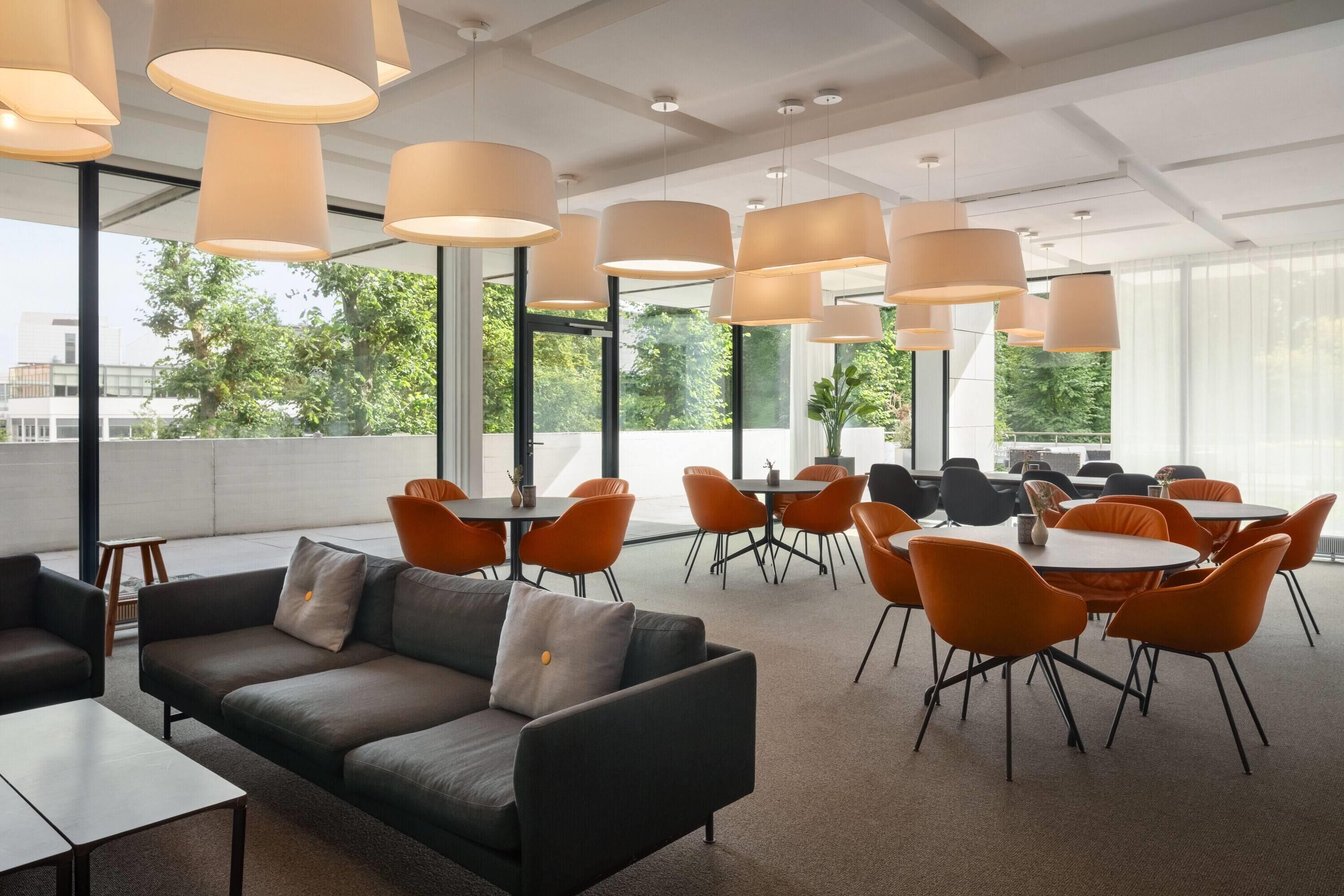 A modern conference room with a black leather couch, orange chairs, and large pendant lights.
