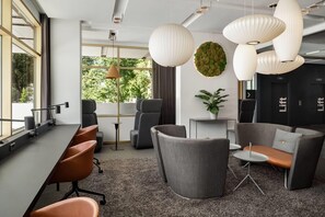 A modern office space with a long conference table, grey and orange chairs, and a seating area with a sofa and armchairs.