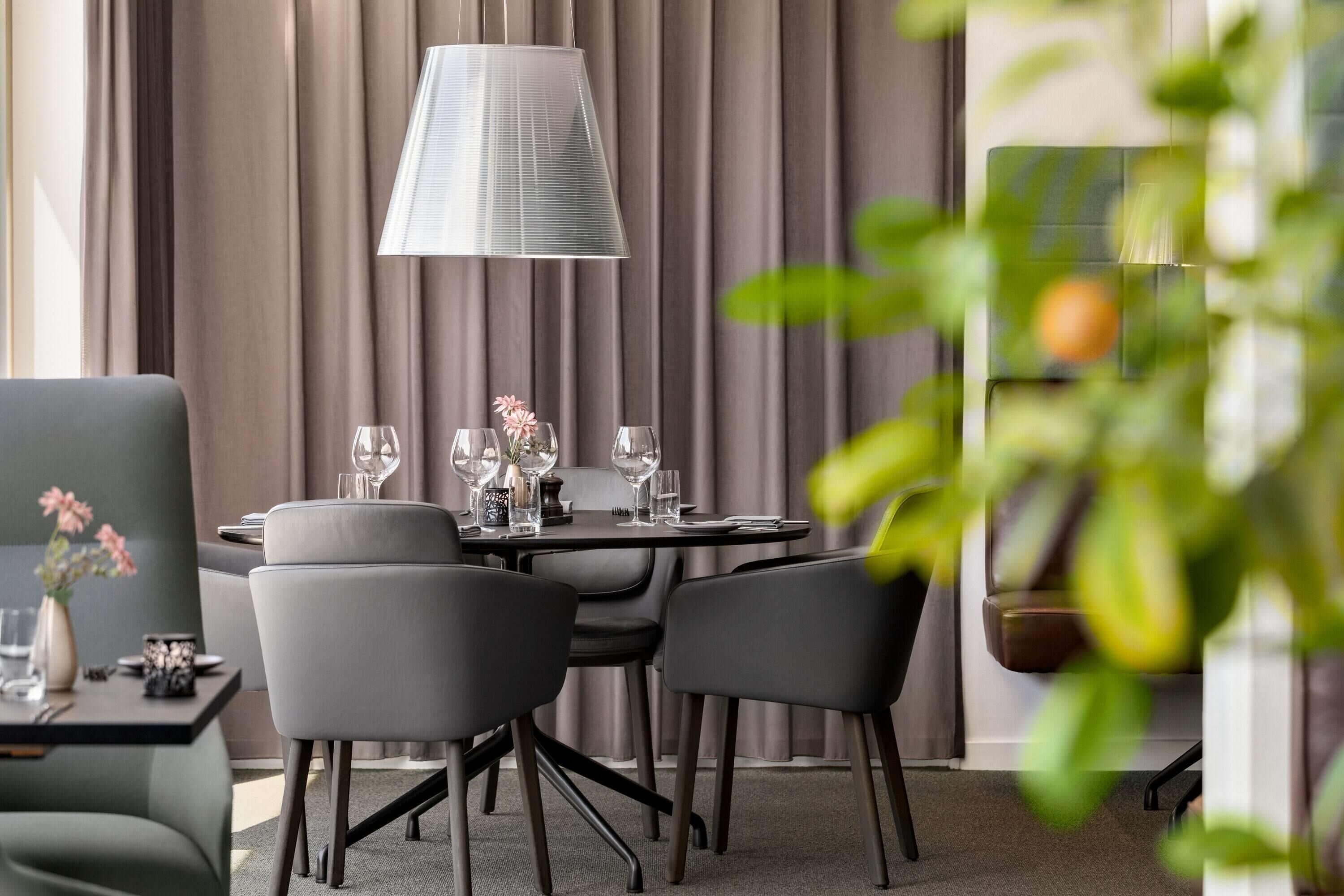 A modern dining area with a round table, grey chairs, and a large lamp.