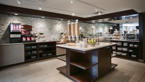 A modern breakfast area with a coffee machine, self-serve beverage dispensers, and a variety of food options.