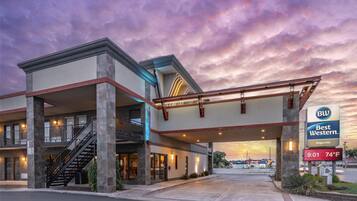 A hotel with a modern architectural design, featuring a prominent entrance, a staircase, and a sign indicating the name and temperature.